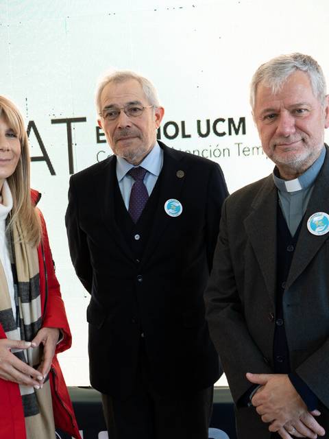Tres personas posan juntas en un evento, con un fondo que incluye un logo y el nombre de una institución.