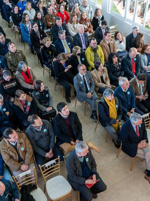 Una gran multitud de personas sentadas en un evento dentro de un salón iluminado.