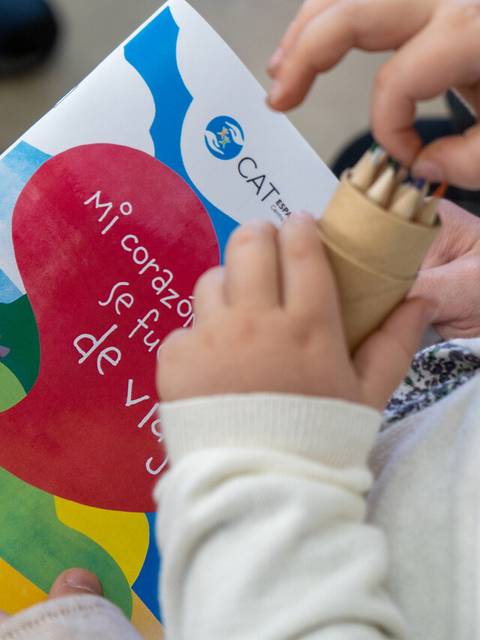 Una niña sostiene un cuaderno titulado 'Mi corazón se fue de viaje' y un soporte con lápices de colores.