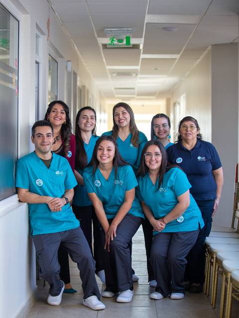 Un grupo de ocho personas sonrientes vestidas con uniformes en un pasillo luminoso.
