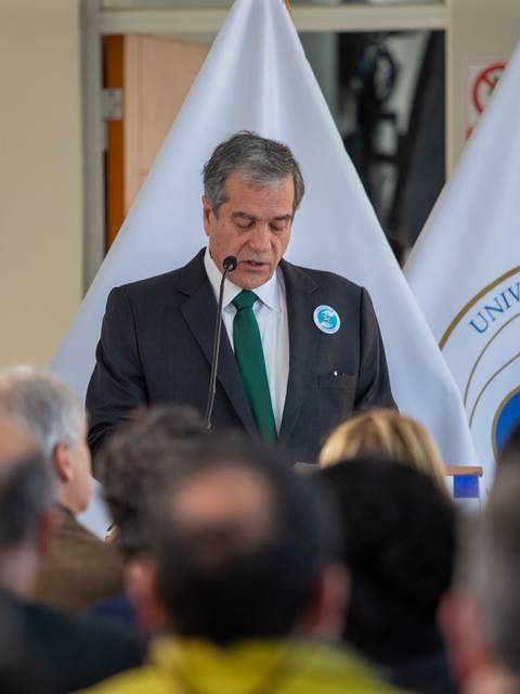 Un hombre habla en un evento en la Universidad Católica ante un público atento.