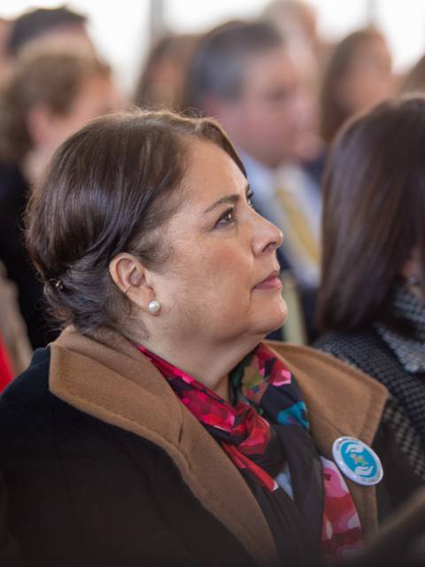 Un grupo de personas escuchando atentamente en un evento, destacando a una mujer con un abrigo oscuro y una bufanda colorida.