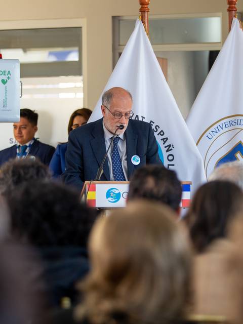 Un hombre habla en un evento formal mientras varias personas lo observan.