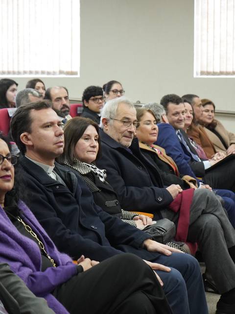 Una audiencia sentada en un salón, observando atentamente hacia el frente.