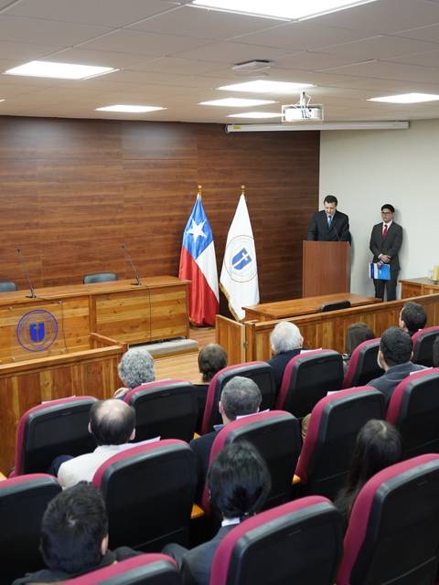 Una sala de conferencias con un podio y una audiencia sentada en sillas rojas.