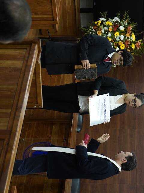 Un hombre está siendo juramentado en un entorno formal mientras dos personas lo observan.