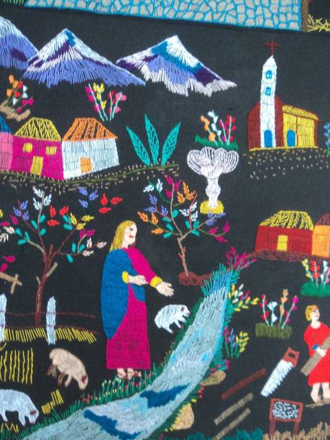 Una colorida escena de una aldea con montañas, casas, personas y animales en un paisaje rural bordado.