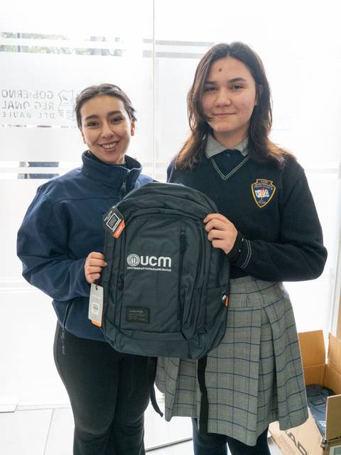 Dos estudiantes sonrientes sosteniendo una mochila en un entorno escolar.