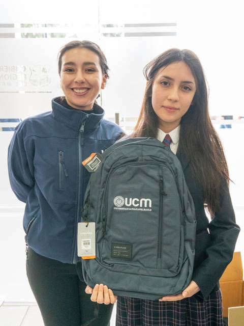 Dos mujeres sonrientes, una de ellas sosteniendo una mochila con el logo de la UCM.