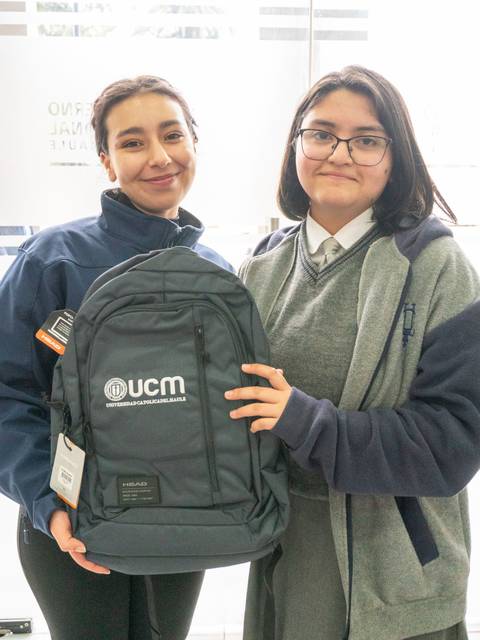 Dos personas sonríen mientras sostienen una mochila con el logo de UCM.