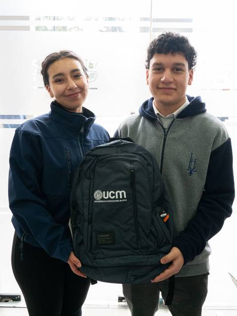 Dos jóvenes sonrientes sosteniendo una mochila, en un ambiente luminoso.