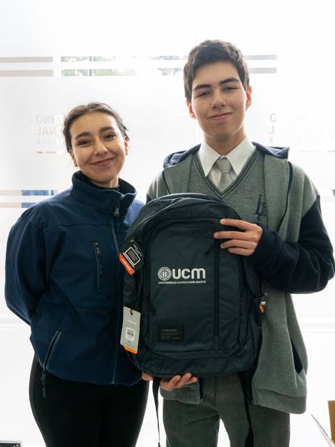 Dos jóvenes sonrientes posan sosteniendo una mochila con el logo de UCM.