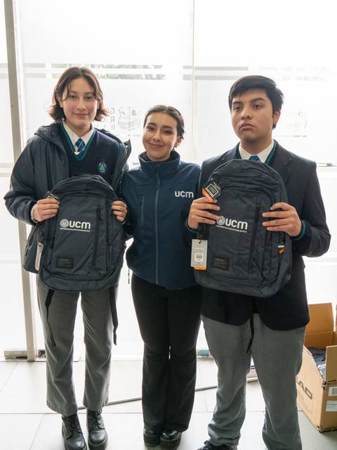 Tres personas posan con mochilas de la UCM en un ambiente interior.