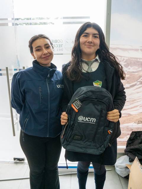 Dos jóvenes posan sonrientes, una de ellas sostiene una mochila con el logo de UCM.