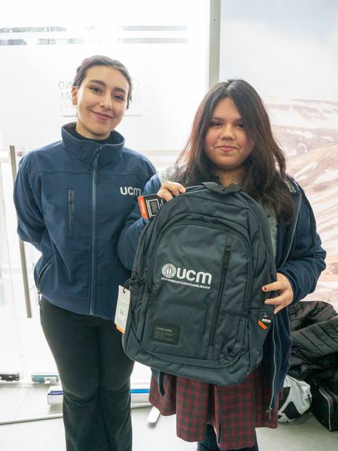 Dos personas posan juntas, una de ellas sostiene una mochila con el logotipo de UCM.