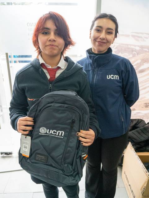 Dos personas de pie, una sosteniendo una mochila con el logo de UCM, en un entorno dentro de un edificio.