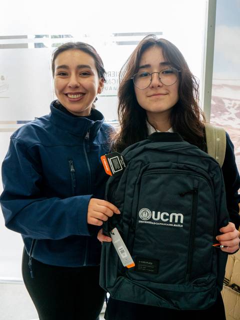 Dos jóvenes sonrientes posan con una mochila en un ambiente luminoso.