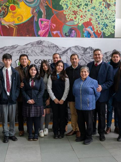 Un grupo de personas posando en un interior con un fondo colorido y una fotografía de montañas.