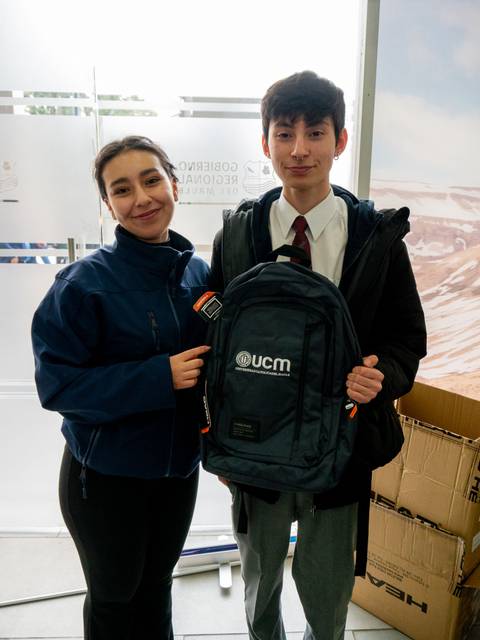 Dos jóvenes posan con una mochila en un lugar interior.