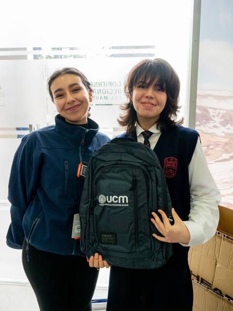 Dos adolescentes posan con una mochila en un entorno interior.