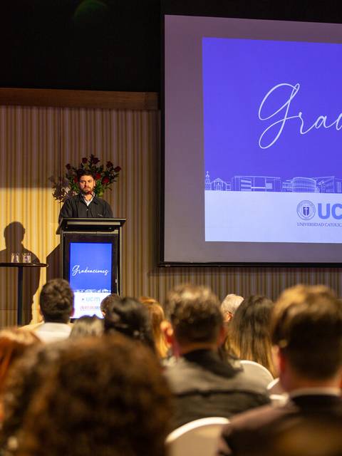 Ceremonia de graduación en un auditorio con un ponente frente a una pantalla.