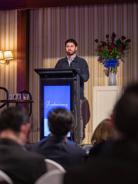 Un hombre se encuentra en un podio hablando ante una audiencia en un evento de graduación.