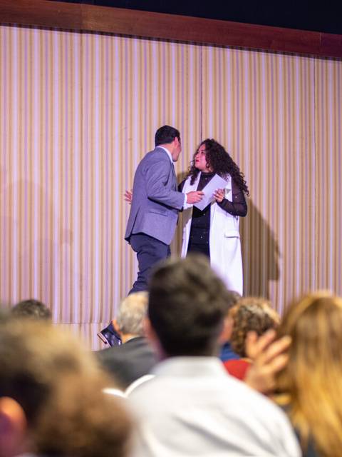 Un hombre y una mujer se abrazan en un escenario durante un evento formal.