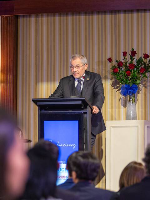 Un hombre de pie en un podio hablando en un evento formal frente a una audiencia.