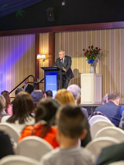 Un orador se presenta en un evento frente a una audiencia atenta en un salón decorado con flores.