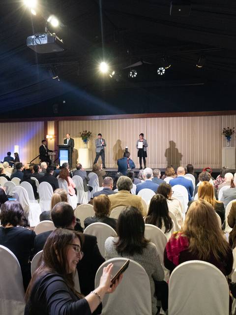 Una multitud de personas asiste a un evento en un salón con sillas blancas dispuestas en filas.