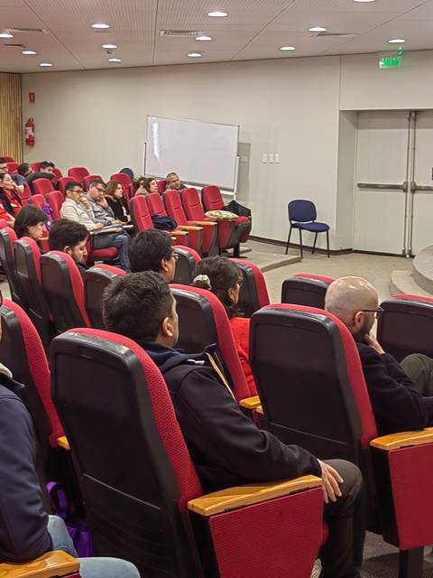 Una conferencia en un auditorio con un gran número de asistentes sentados frente a una presentación en pantalla.