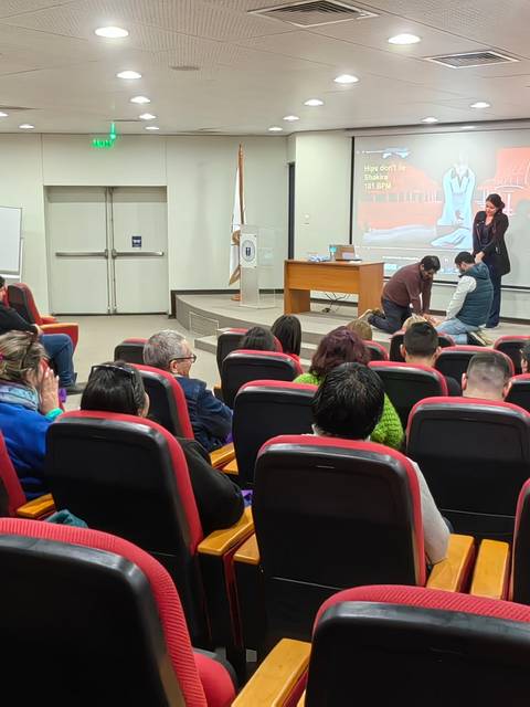 Una conferencia con asistentes en un salón equipado con asientos rojos y una pantalla al fondo.