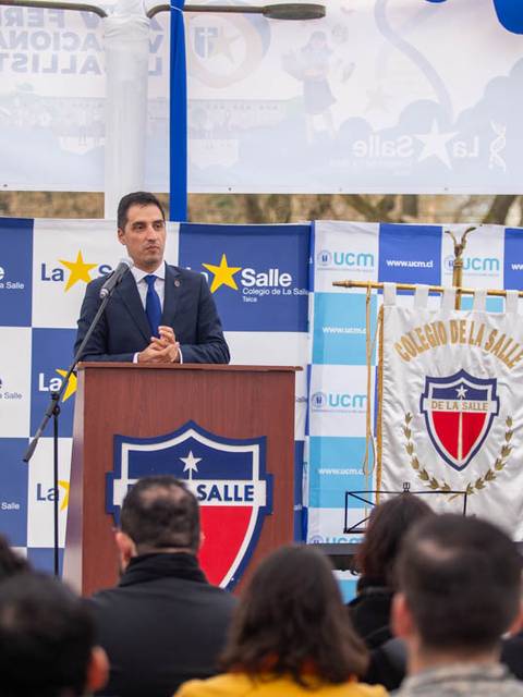 Un hombre habla desde un podio en un evento de La Salle, con banderas de Chile y decoraciones de la institución al fondo.