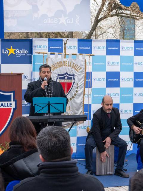 Un grupo de músicos realiza una presentación en un evento al aire libre con un fondo decorado con logos de La Salle.