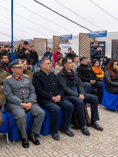 Una multitud de personas, incluyendo a miembros de las fuerzas armadas y civiles, se sientan en un evento bajo una carpa.