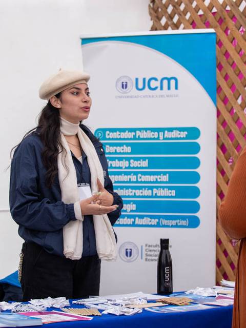 Una mujer interactúa con otra en un stand informativo de la UCM sobre diversas carreras profesionales.