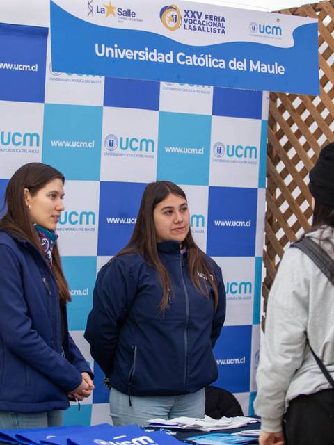Una feria educativa con representantes de la Universidad Católica del Maule interactuando con visitantes.