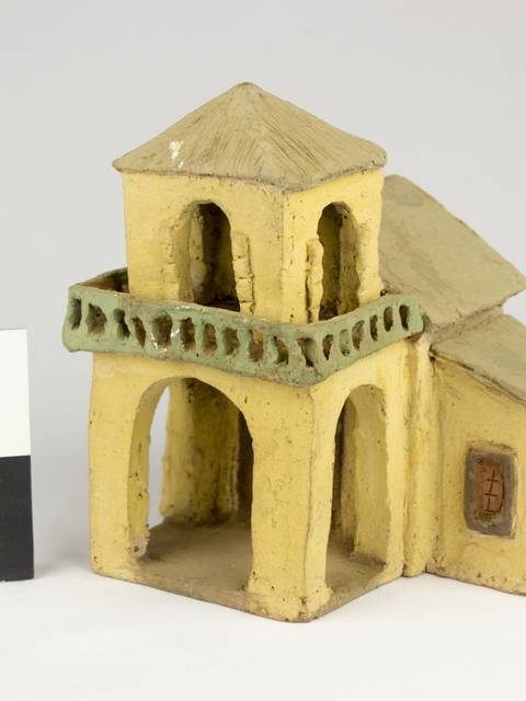 Una pequeña maqueta de un edificio de dos pisos con un balcón y un tejado, hecha de material marrón claro.