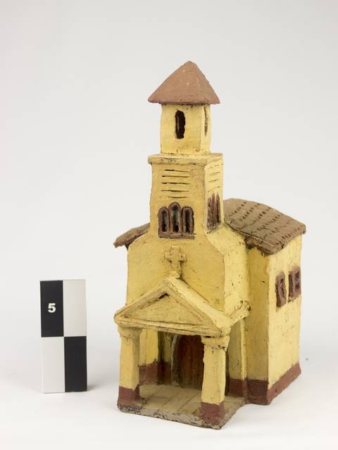 La imagen muestra una maqueta de una iglesia de color amarillo con detalles en marrón.