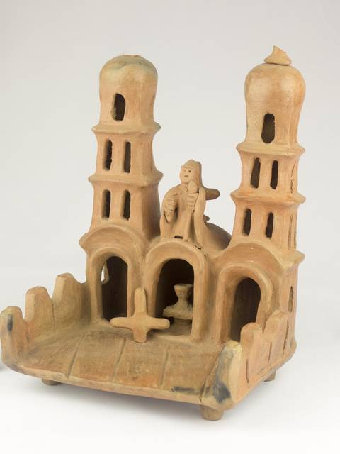 Una figura de cerámica que representa un edificio con dos torres y una figura humana en el centro.