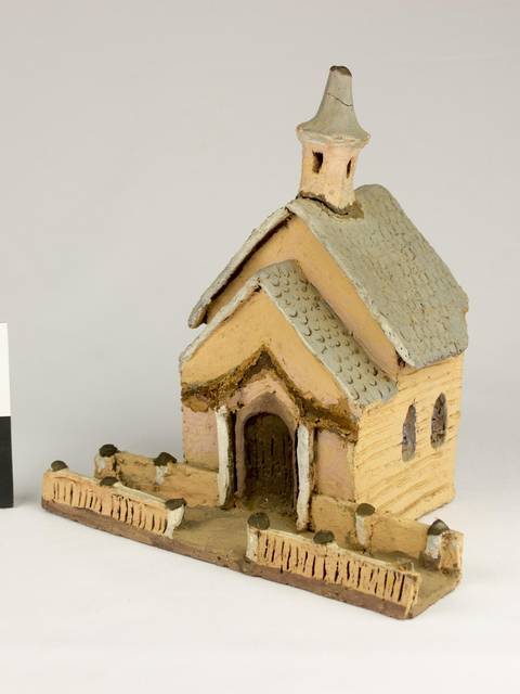 Una maqueta de una pequeña iglesia de madera con un tejado a dos aguas y una torre en la parte superior.