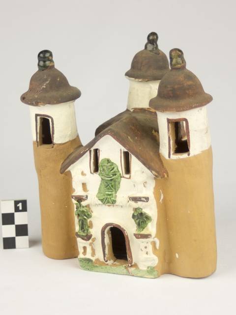 Una figura de cerámica que representa un edificio con torres y detalles en verde.