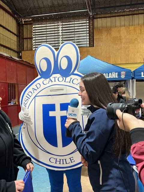 Una estudiante conversa con una mujer frente a un personaje disfrazado de una mascota universitaria en un evento.
