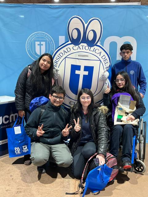 Grupo de estudiantes posando sonrientes frente a un stand de la Universidad Católica del Maule.