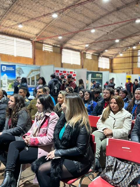 Un grupo de personas sentadas en sillas, esperando en un evento dentro de un recinto cerrado.