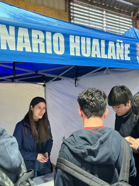 Un grupo de jóvenes se encuentra en una feria frente a un stand que dice 'Liceo Politécnico Hualañé'.