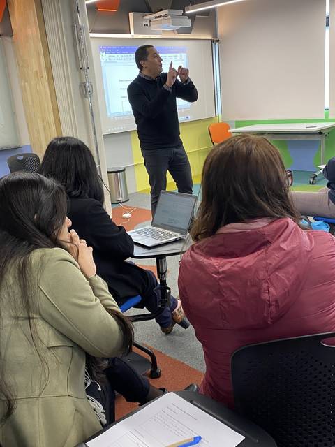Un grupo de personas asiste a una presentación en una sala moderna con pantallas y mobiliario colorido.