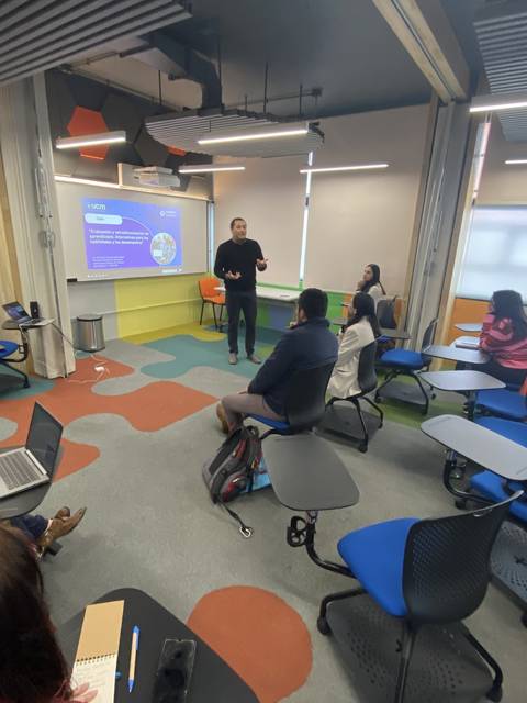 Un grupo de personas asiste a una presentación en un aula moderna y colorida.