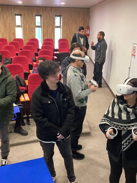 Un grupo de personas utiliza gafas de realidad virtual en un salón con asientos rojos.