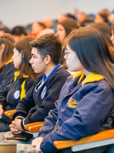 Un grupo de estudiantes sentados en un evento, prestando atención al ponente.